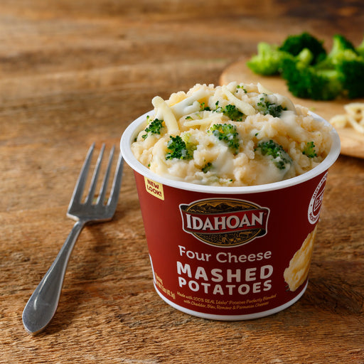 Idahoan® Four Cheese Mashed Potatoes Cup made on a table with broccoli and cheese